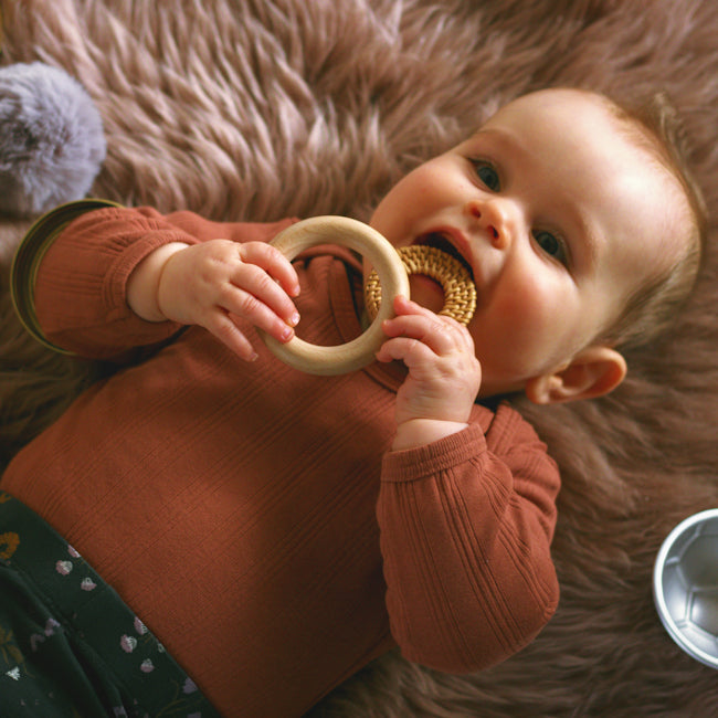 A happy baby lying on a playmat playing with open-ended heuristic play toys.