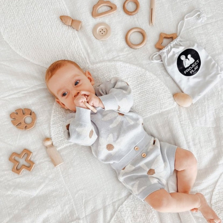 Baby lying on a playmat playing with open-ended loose parts toys